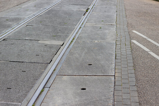 Concrete tram tracks embedded in pavement with adjacent cobblestone sidewalk and asphalt road, showcasing urban infrastructure in a city setting
