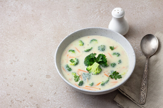 Homemade creamy broccoli soup with potatoes carrots and parsley in ceramic bowl on light textured background