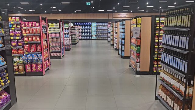 Interior view of a modern, brightly lit supermarket aisle flanked by well-stocked shelves with a clean floor, creating an organized shopping space.