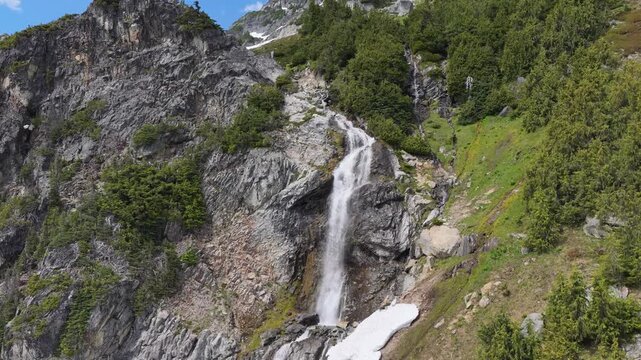Majestic Mountain Waterfall Cascading Through Lush Green Forests and Snow Patches in British Columbia, Canada