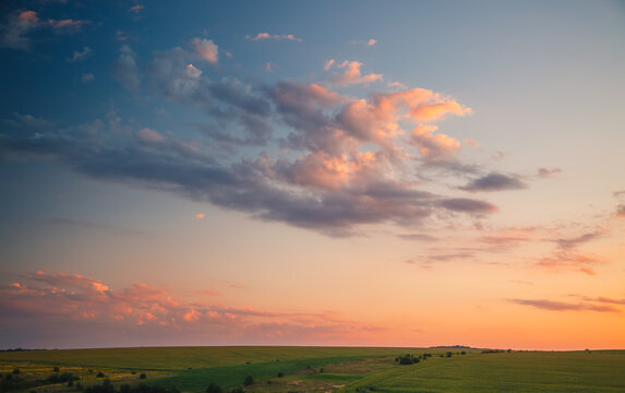 Colorful clouds drift over a serene landscape at sunset, painting the sky in hues of orange and pink, creating a magical and cozy atmosphere.