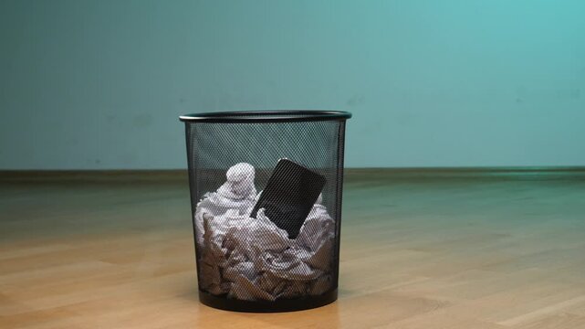 Hand is throwing a smartphone into a trash bin filled with crumpled paper, symbolizing a digital detox, addiction break, or the disposal of old e waste and unwanted device