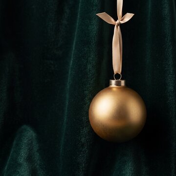 Elegant gold Christmas bauble hanging by a ribbon against a dark emerald green velvet background