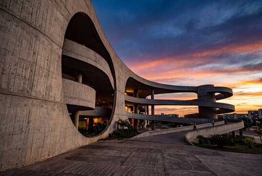 Modernist brutalist concrete architecture with spiral ramps and circular cutouts at sunset