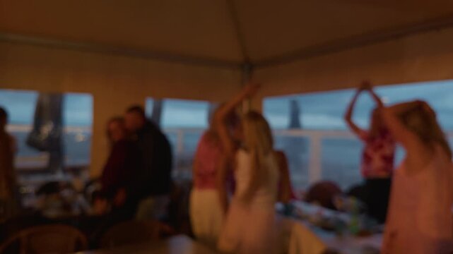 Blurred group dancing inside evening party room with ocean view through wide windows