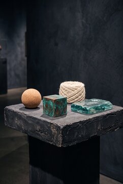 Minimalist art installation featuring a sphere, cube, twine, and glass on a dark stone pedestal