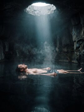 Man floating in a dark cave pool under a dramatic beam of light