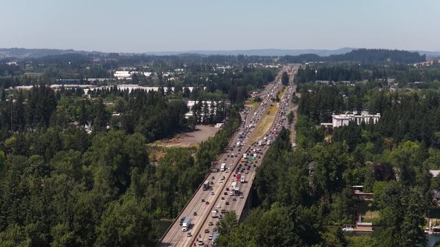 Aerial of Interstate 5 in forested suburban landscape near Wilsonville Oregon with heavy traffic on the multilane freeway on sunny summer day