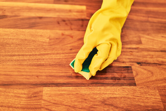 Scrubbing a hardwood floor with a sponge and rubber gloves