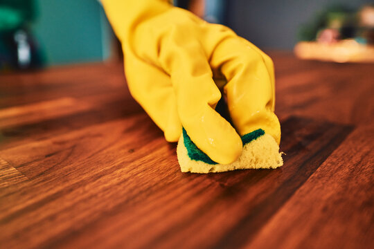 Cleaning a wooden surface with a sponge in rubber gloves