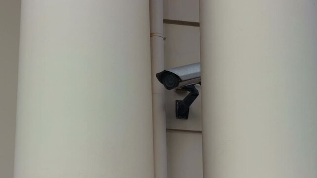 Surveillance camera mounted between tall concrete pillars on building facade with narrow view of security monitoring