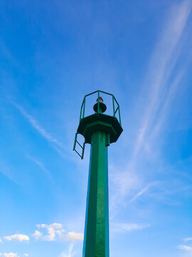 View of tall, green metal construction, point lighthouse against clear blue sky