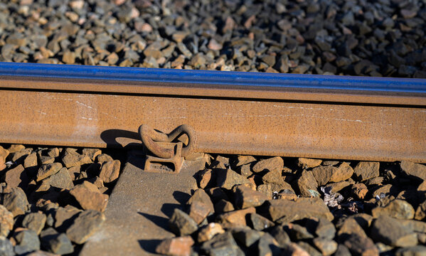 Rusty railway rail fastener closeup on gravel ballast.