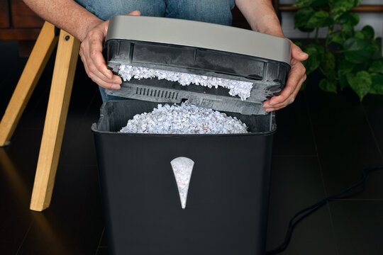 Mid shot showing person holding shredder motor and blade unit above black bin filled with shredded paper showing full capacity