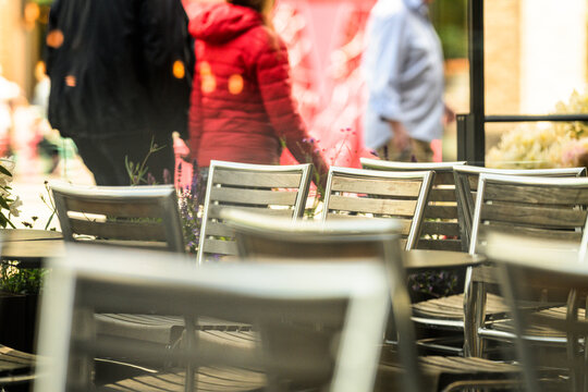 Outdoor cafe terrace chairs with blurred pedestrians in city setting.