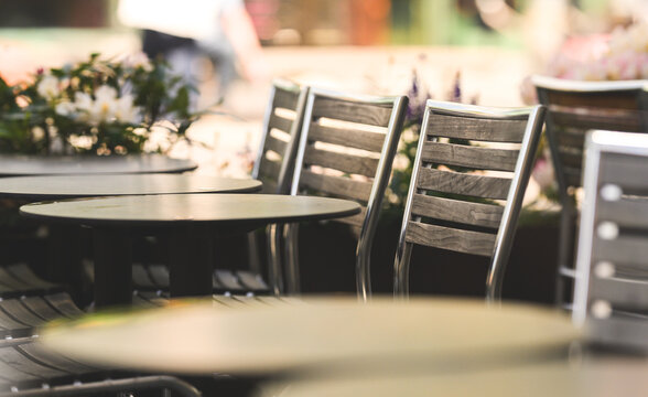 Empty outdoor cafe chairs and tables with soft urban background.