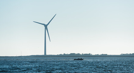 Offshore wind turbine near coastline with small motorboat. © Trygve