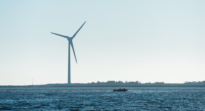Offshore wind turbine near coastline with small motorboat.