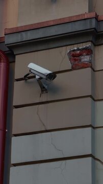 Security camera mounted on cracked building wall with damaged plaster and exposed brick detail