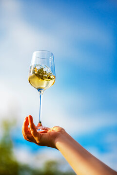 Sauvignon Blanc glass swirling in hand against clear blue sky outdoors. Dynamic liquid motion and high end product presentation concept.