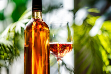 Obraz premium Rose wine bottle close up with glass on background. Tropical resort lounge terrace card and premium alcohol brand design concept.