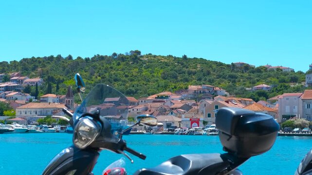 Scooter parked at marina overlooking picturesque croatian town. Scenic view of a beautiful coastal town with traditional houses and a vibrant blue sea, seen from a harbor with a scooter parked