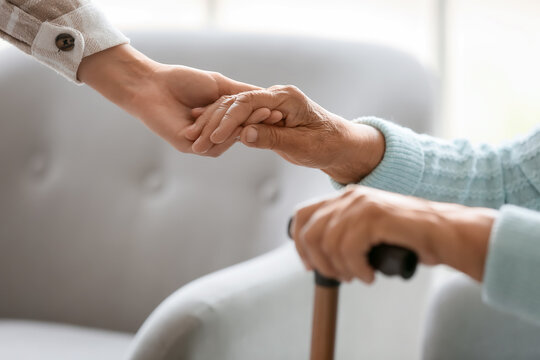 Senior woman with stick and daughter holding hands at home, closeup