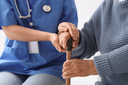 Nurse and senior woman with stick holding hands in clinic, closeup