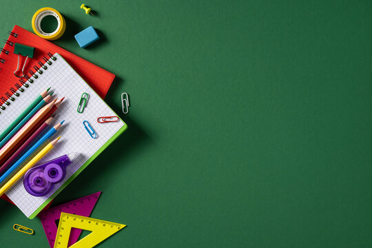 Back to school supply arrangement with colored pencil notebook ruler and paperclip on green background