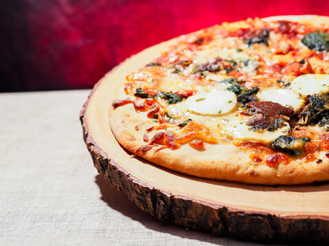 Cooked goat cheese and red onion chutney pizza with spinach and fine herbs and spice on wooden board and simple table cloth and red hot background. Premium Italian style meal made with sourdough.