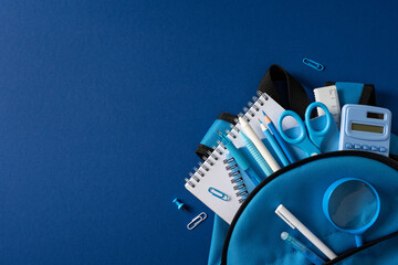 Fototapeta premium Back to school backpack with blue stationery, notebook, pencil, scissors and calculator arranged on blue background