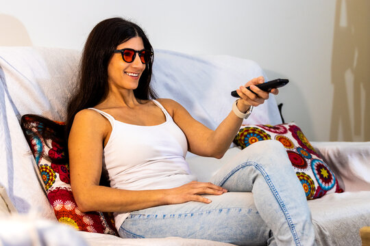 Woman with red blue light blocking goggles watching tv, holding remote control