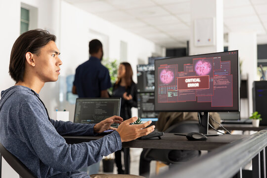 Young programmer having a stressed expression while seeing a critical error message and data breach pop ups on his computer monitor, indicating a serious cyber attack or system failure.