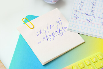 Obraz premium Sticky note with math formulas and notebook on light background, closeup