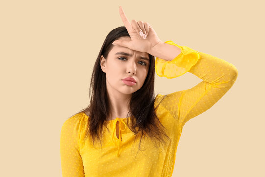 Upset young woman showing loser gesture on beige background, closeup