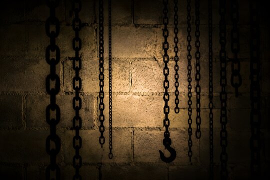 Dark backlit silhouettes showing heavy metal dangling chains positioned against a dimly lit cinderblock wall