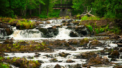 Panorama of multiple waterfalls cascading with greenery and bridge in background © Stephanie