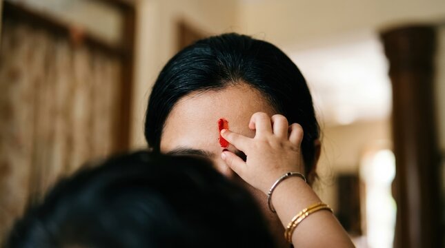 Indian mother and child bonding during traditional tilak ceremony at home, close up of vermilion mark on forehead