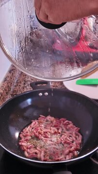 Slow motion shot of a man cooking traditional Italian pasta sauce, stirring sizzling pancetta cubes with a wooden spoon in a hot wok pan on the kitchen stove, preparing a Mediterranean meal