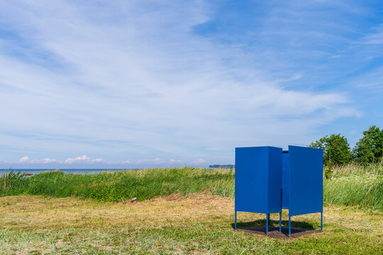 Blue beach changing cabin on grassy Baltic Sea shore under summer sky