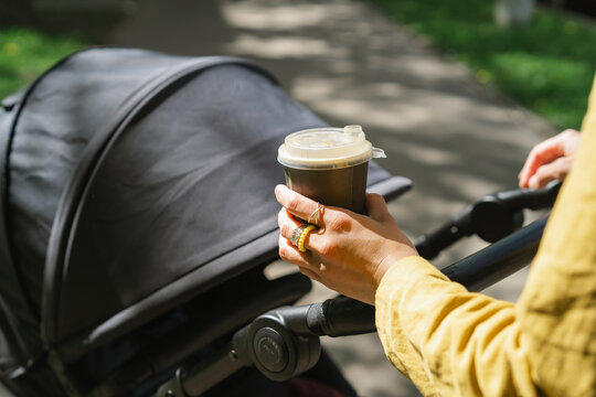 Close-up of a woman holding a cup of coffee while pushing a stroller in a park on a sunny day