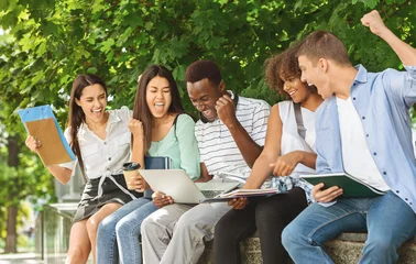 Exam Results. Group Of Joyful International Students Celebrating Success With Laptop Outdoors, Checking Their Test Scores Online © Prostock-studio