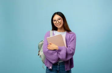 Academic education. Asian lady with backpack and notebooks smiling at camera on blue studio background. Korean woman university student ready to start education © Prostock-studio