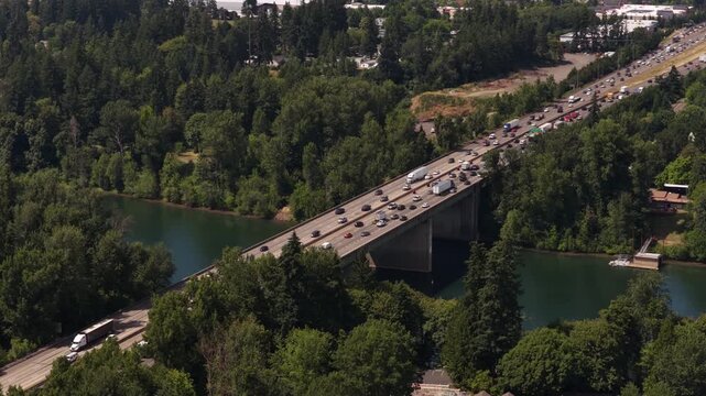 Aerial of Interstate 5 over WIllamette River in Wilsonville Oregon with heavy traffic on the bridge and forested riverbank in summer