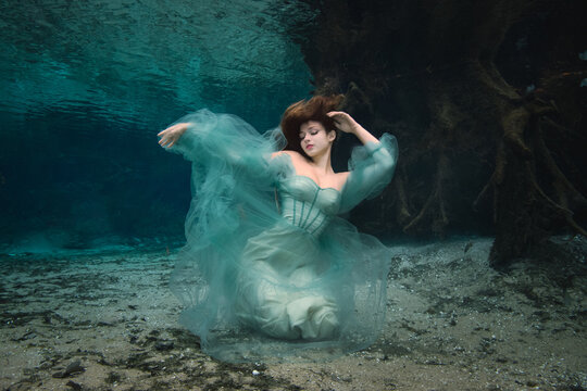 Young woman in a turquoise off shoulder evening gown kneeling underwater on a riverbed, Florida, USA