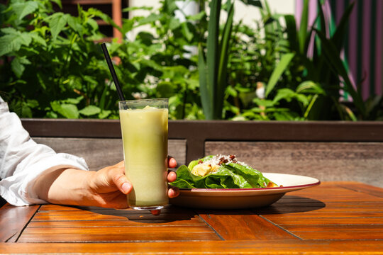Close-up of a woman with an iced matcha latte and a salad sitting at a table at an outdoor cafe