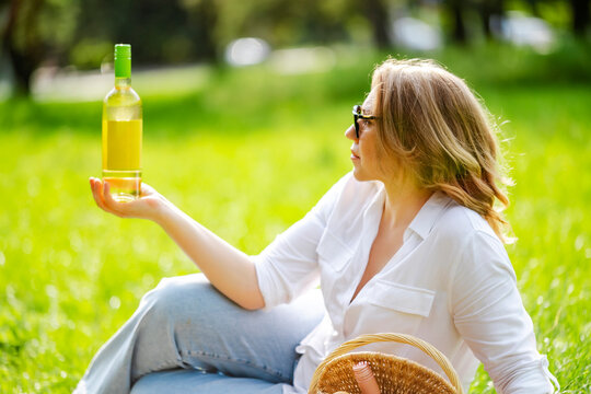 Woman expert holding Sauvignon Blanc bottle at summer picnic on grass. Outdoor wine degustation and weekend relaxation concept.