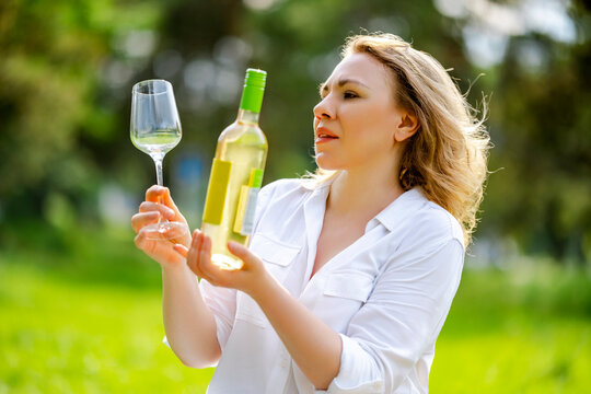 Woman expert holding Pinot Grigio bottle and glass on outdoor evaluation. Sommelier tasting and luxury outdoor lifestyle concept.