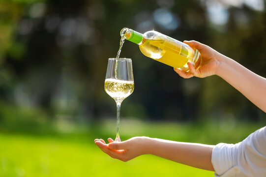 White wine pouring from bottle into glass, outdoors at summer party. Elegant garden celebration and premium alcohol concept.