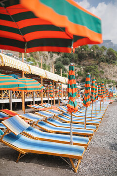 Close-up of a row of striped sun loungers and beach umbrellas lined up on a pebble beach on the Amalfi Coast, Positano, Campania, Italy